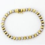 An 18ct yellow and white gold tennis bracelet set with brilliant cut diamonds, L. 19cm.