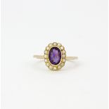 A yellow metal (tested minimum 9ct gold) ring set with an oval cut amethyst surrounded by seed