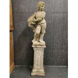 A concrete garden figure of a boy carrying a basket of fruit on a concrete plinth, overall H.