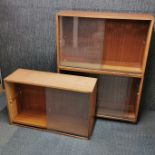 A teak shelving unit on castors with glass sliding doors together with two further teak wall mounted