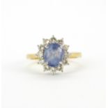 An 18ct yellow gold cluster ring set with an oval cut Ceylon sapphire surrounded by diamonds, (K).