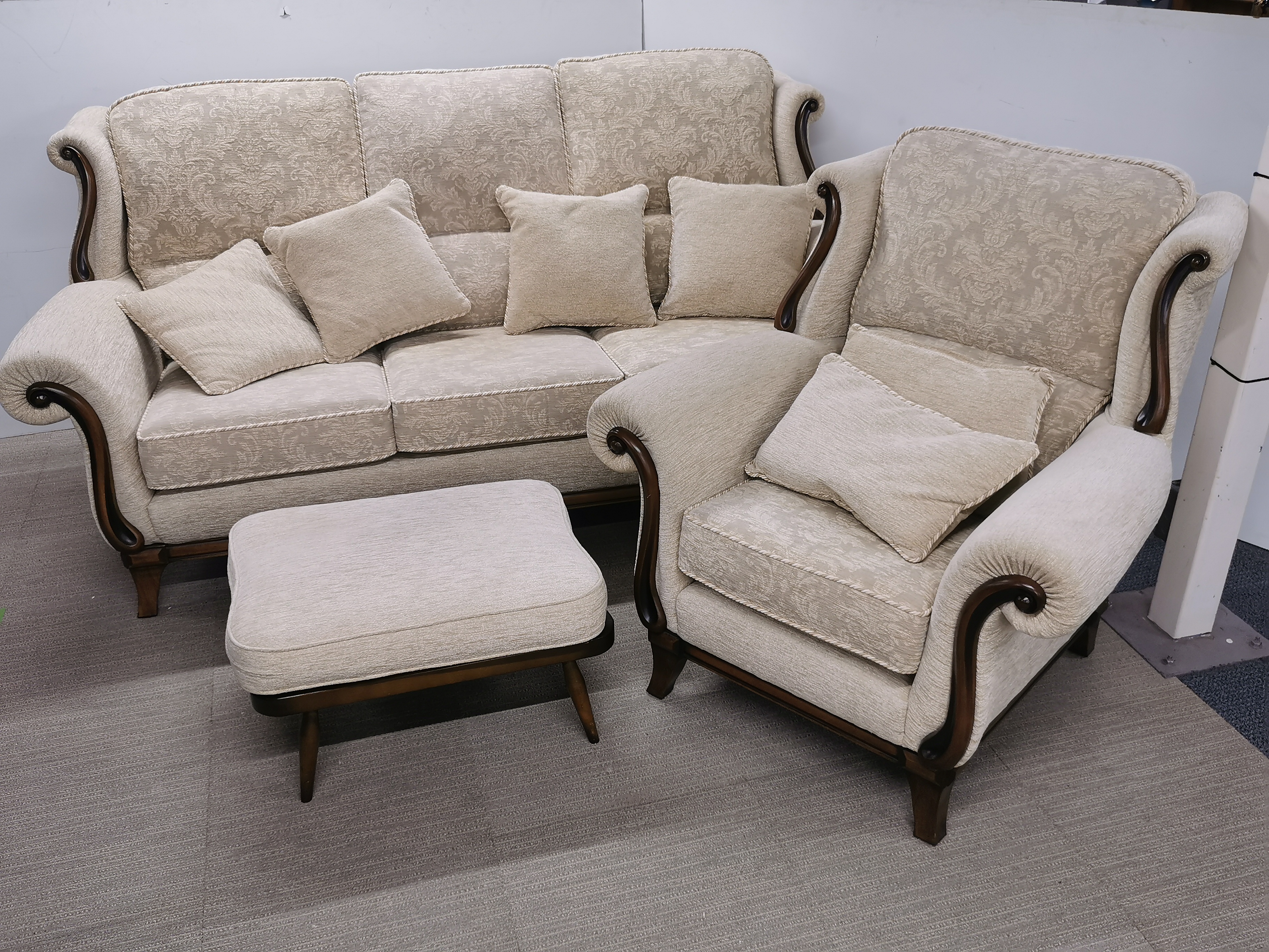 A heavy quality cream upholstered settee with a matching armchair and an Ercol footstool.