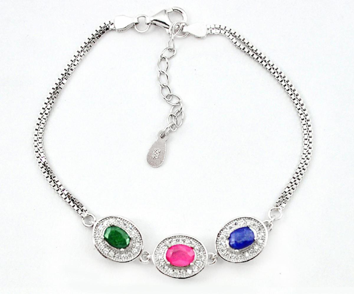 A 925 silver bracelet set with an oval cut sapphire, ruby and emerald, surrounded by white stones,
