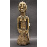 A West African carved wooden sculpture with unusual highlights on the body and cowrie shell eyes.