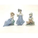 A group of three Nao porcelain figurines of children, two with boxes.