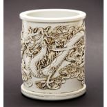 A Chinese Blanc de Chine porcelain brush pot, relief decorated with a dragon playing with a