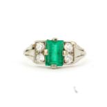 A yellow metal (tested 18ct gold) ring set with a baguette cut emerald and four old brilliant cut