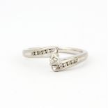 An 18ct white gold crossover ring set with a brilliant cut diamond and diamond set shoulders, (O.