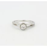 An 18ct white gold halo ring set with brilliant cut diamonds and diamond set shoulders, center stone