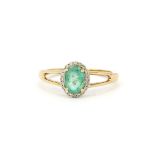 A hallmarked 9ct yellow gold (stamped 10K) ring set with an oval cut emerald surrounded by diamonds,