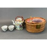 A mid 20th century Chinese porcelain tea pot and two cups in an insulated bamboo carrying basket, W.