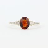 A 9ct yellow gold ring set with an oval cut hessonite garnet and diamond set shoulders, (U).