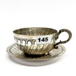 A large French white metal Belle Epoque teacup and saucer, stamped 'Lauzolle', saucer dia. 16cm.