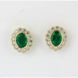 A pair of 18ct white gold (stamped 750) cluster earrings set with oval cut emeralds and brilliant