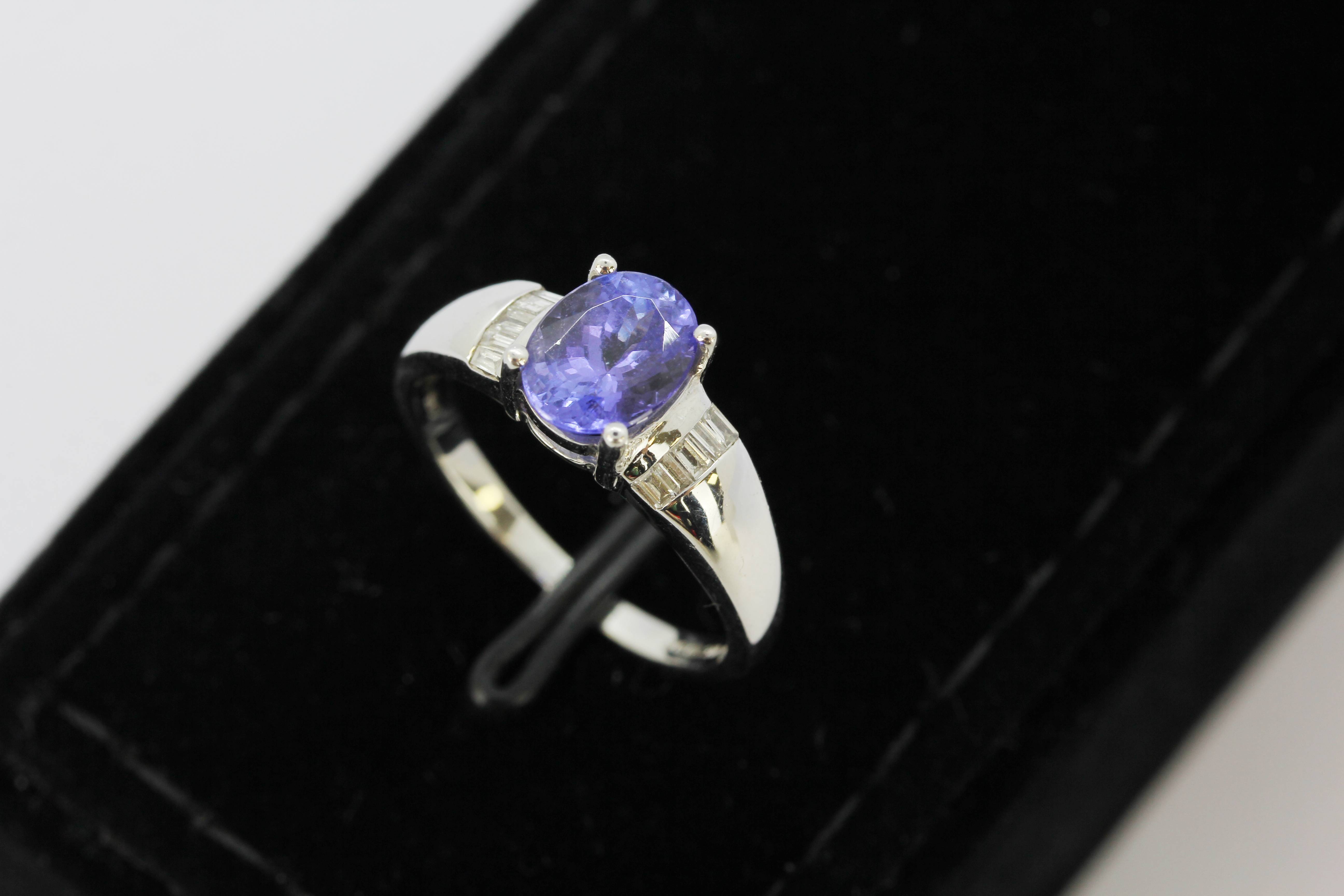 An 18ct white gold ring set with an oval cut tanzanite and diamond set shoulders, (M.5).