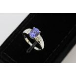 An 18ct white gold ring set with an oval cut tanzanite and diamond set shoulders, (M.5).