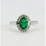 An 18ct white gold (stamped 750) ring set with an oval cut emerald and brilliant cut diamonds, (N.