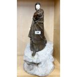 A superb early 20th century bronze figure of a woman with a coat, mounted on a carved stone base