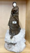 A superb early 20th century bronze figure of a woman with a coat, mounted on a carved stone base