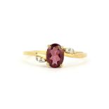 A 9ct yellow gold (stamped 375) ring set with an oval cut rubellite garnet and white stone set