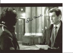 James Bond Oliver Skeete signed 10x8 black and white photo with Pierce Brosnan. Good condition.
