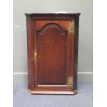 A Georgian oak corner cupboard with single fielded and arched panel door and H shaped brass