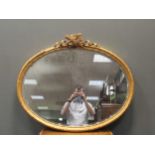 An oval gilt wall mirror surmounted by classical ribbons and trophies 80 x 94cm