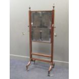 A Regency mahogany cheval mirror, the rectangular plate within a pair of brass swivel action