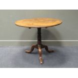 An elm topped circular tripod table, 19th century, the circular tilt-top over a turned column