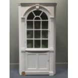 A white painted corner cupboard, the moulded cornice above a glazed arched cupboard door flanked
