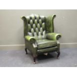 A wing back armchair upholstered in green faux-leather on short cabriole legsHawks Club Cambridge