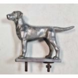 A white metal car mascot in the form of a dog