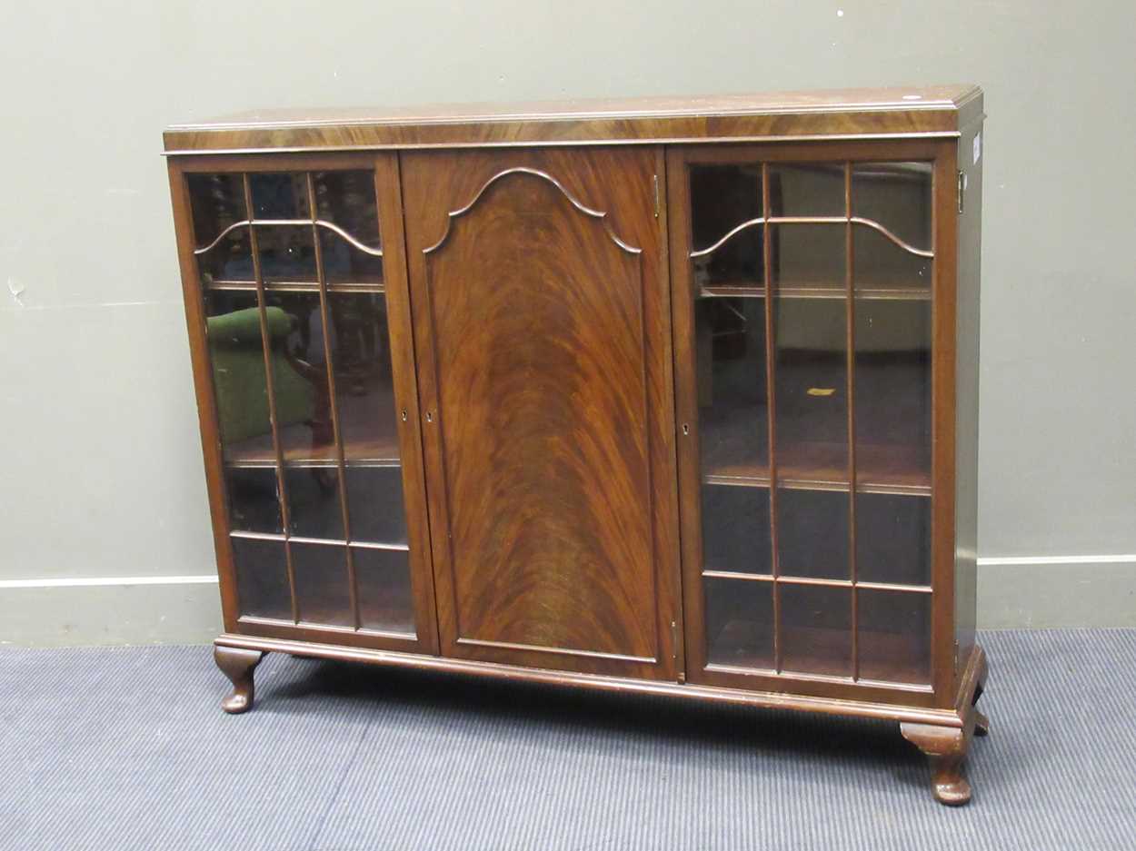 A 1920s mahogany low bookcase cabinet with central cupboard door flanked by a pair of glazed