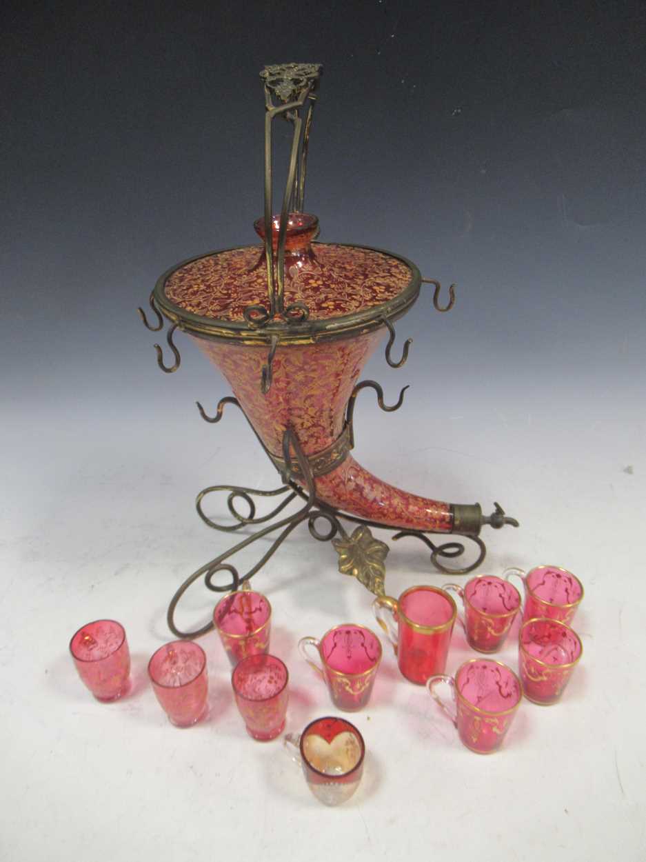 A cranberry glass and gilt cornucopia drinks dispenser with matched cranberry glass miniature