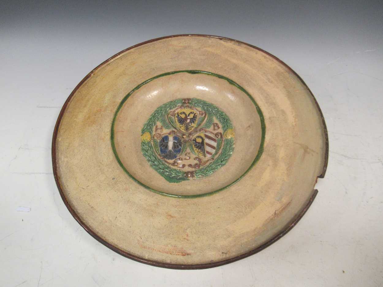 A continental pottery plate, the centre moulded with coats of arms, 35cm diameter