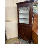 A Georgian oak two piece floor standing corner cabinet, the base with three drawers above two arched