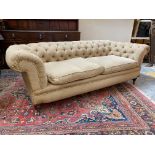 A late Victorian Howard style button back upholstered chesterfield sofa raised upon turned front