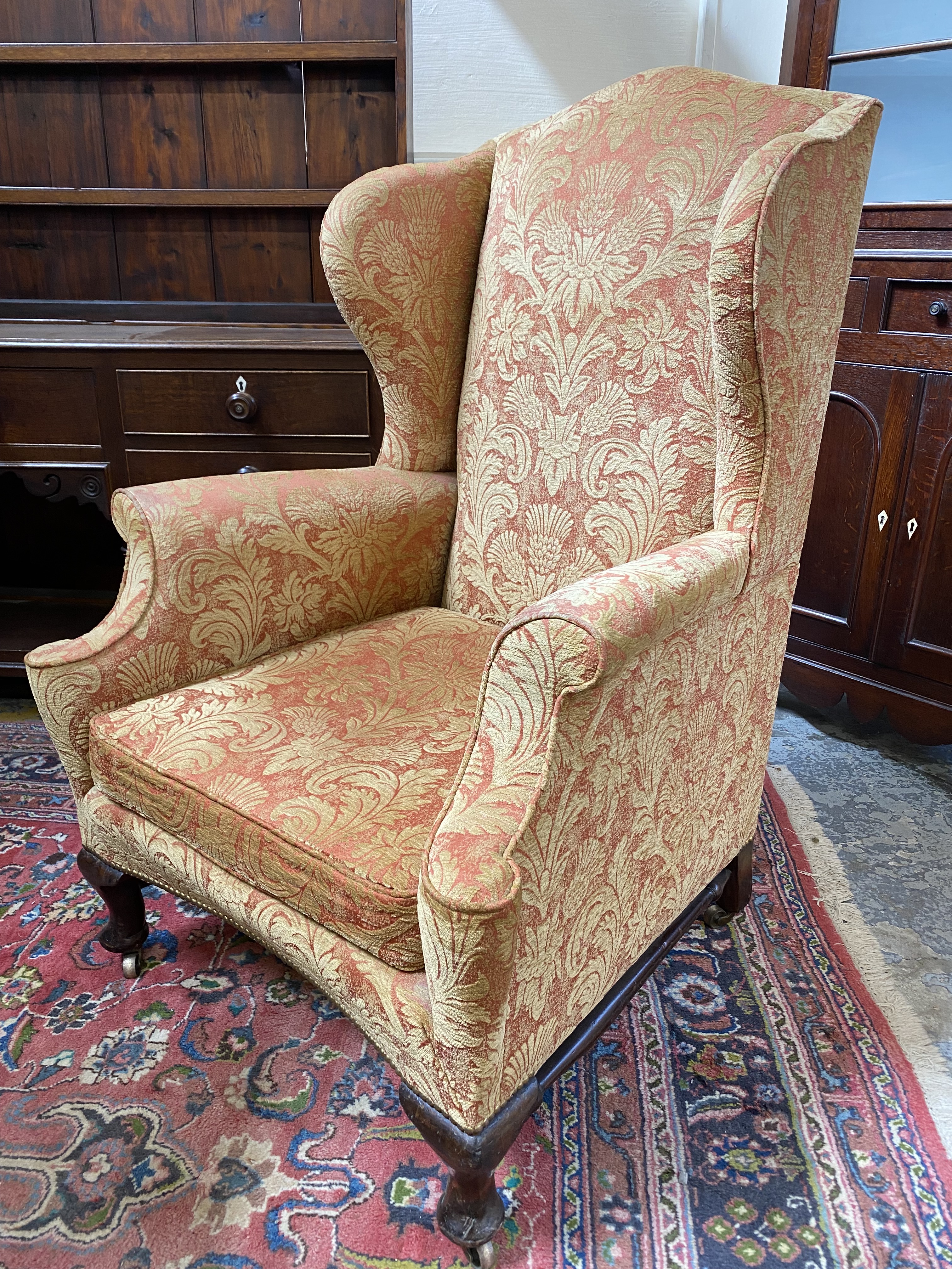 An upholstered wing back armchair raised upon mahogany supports, joined by a stretcher, probably