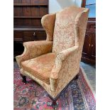 An upholstered wing back armchair raised upon mahogany supports, joined by a stretcher, probably