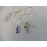 A diamond inset silver cross pendant on a silver chain and a three stone tanzanite pendant on a