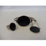 A stylish white metal (probably silver) bangle, pendant and ring, all set with a black stone,