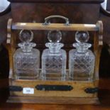 An early 20thC oak Tantalus, comprising three glass decanters, all chipped, locking mechanism,