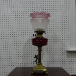 An antique brass columnar Oil Lamp, adorned with figure of Cupid and red glass reservoir, 63cm tall.