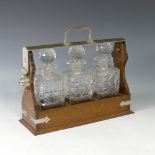 An early 20thC oak three bottle Tantalus, fitted with three cut glass decanters, with keys, W 37cm x