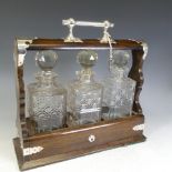 An Edwardian oak Tantalus, with silver-plated handle and mounts, encasing three cut glass decanters,