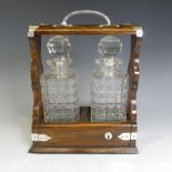 An Edwardian oak Tantalus, with silver-plated handle and mounts, encasing two cut glass decanters,