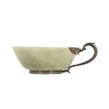 A PALE CELADON JADE CUP WITH A WHITE METAL HANDLE.