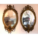 A near pair of gilt framed oval girandoles, each with scrolling crest,