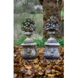 A pair of reconstituted stone garden ornaments modelled as vases of fruit on plinths with moulded