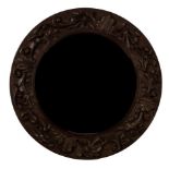 An Arts & Crafts oak circular mirror, the border carved anthemion and foliate scrolls,
